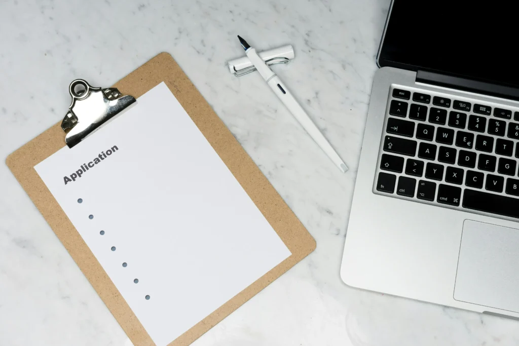A business owner’s laptop and clipboard, preparing to apply for a merchant account.